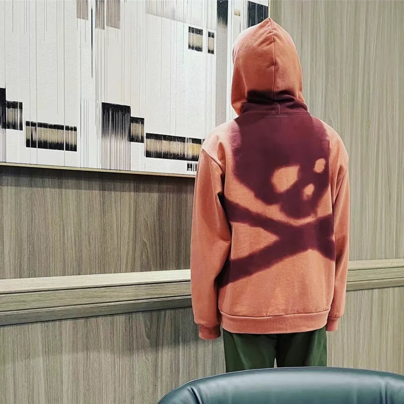 Person wearing a pink hoodie with a shadow design on the back, standing in a room with wooden paneling.